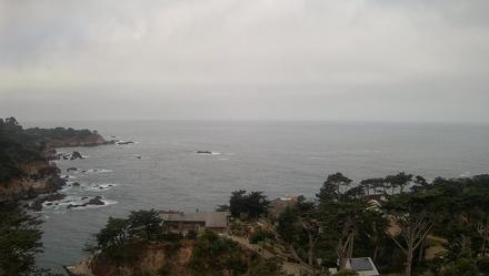 Fixed coastal view over Carmel by the Sea, rocky cliffs, breaking surf and a wide Pacific horizon with vivid sunsets.