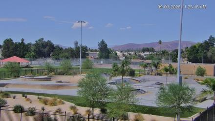 An outdoor concrete skatepark under daylight with various bowls, ridges, and ramps set against clear sky and urban background.