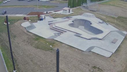 Concrete skate ramps, rails, and bowls under an overcast sky, with skaters’ silhouettes in motion.