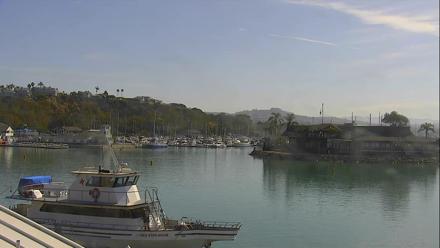 Marina basin with boats moored, harbor docks, and distant coastal hills under soft daylight