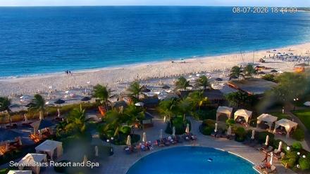 Live view of Grace Bay in Turks and Caicos, turquoise water, white sand, gentle surf and a beachfront resort scene.