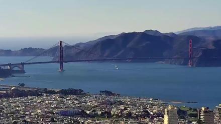 Northwest view of the Golden Gate Bridge over San Francisco Bay with city rooftops and boats seen from a high rise camera.