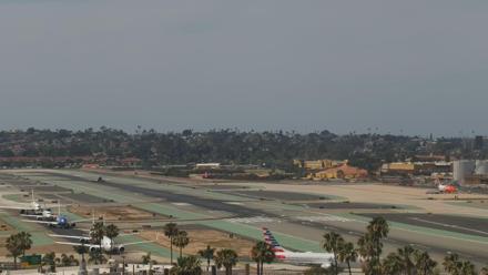 Airport runway and San Diego Bay visible beyond, with several aircraft and waterfront in view